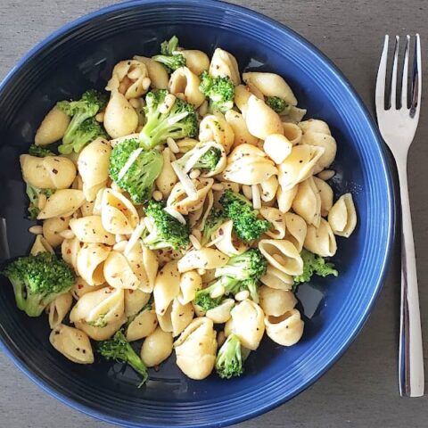 Broccoli and pine nuts studded chickpea pasta served in blue bowl.