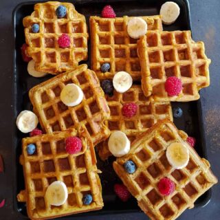 A tray full of vegan and gluten free pumpkin waffles served with fresh berries and maple syrup.