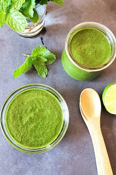 Overhead image of Chutney served in glass bowl and glass jar along with fresh mint leaves.