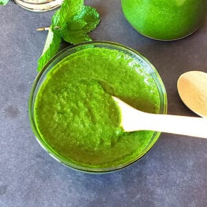 Thick green mint cilantro Indian Chutney served in a glass bowl with wooden spoon.