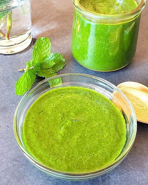 Thick green Indian chutney served in a glass jar.