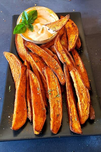 Air fryer sweet potato wedges served on black serving plate with garnishes.