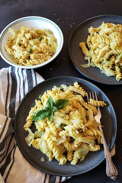 A dinner serving with three plates of cabbage pasta with garnishes.