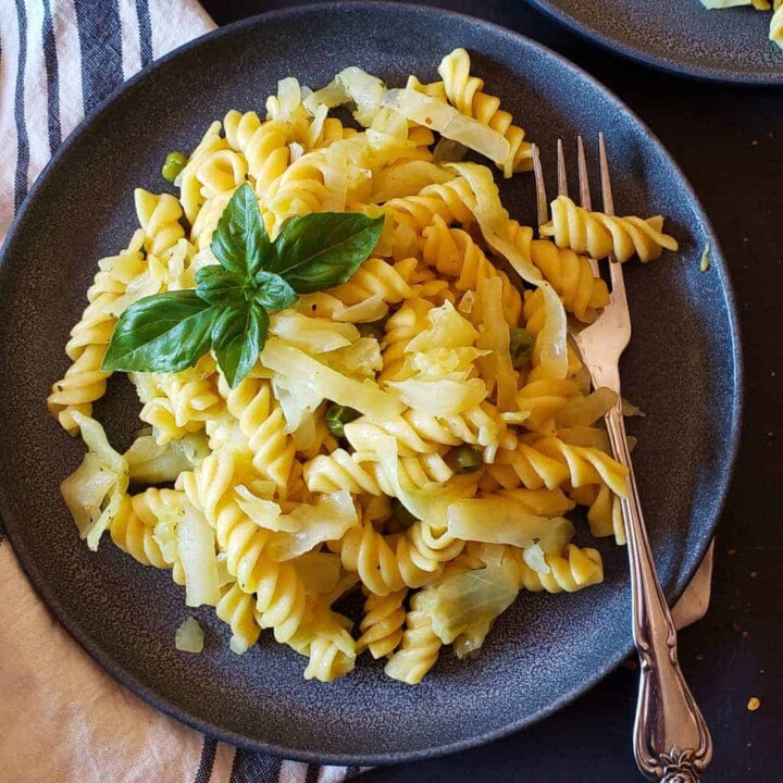 Haluski which is fried cabbage, peas and pasta dish made in Instant Pot and served on black pasta plate with a fork on the side.