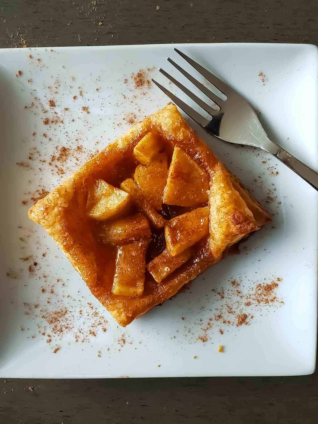 An apple pie puff pastry served with a fork on the white dessert plate.