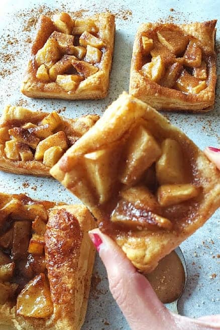 A hand holding beautifully crusted flakey apple pie puff pastry.