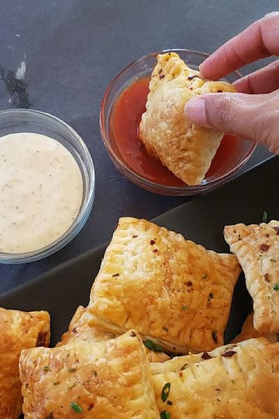 A hand holding a bite sized mushroom puff and dipping in the ketchup.