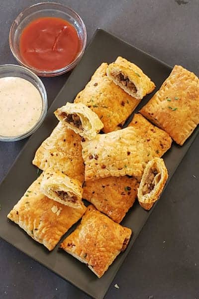 A black serving plate filled with square mushroom puffs along with ketchup and ranch dip.