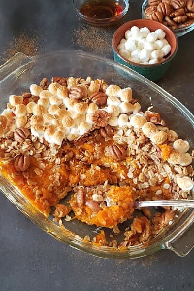 A spoon scooping the sweet potatoes and toasty marshmallows from the baking dish.