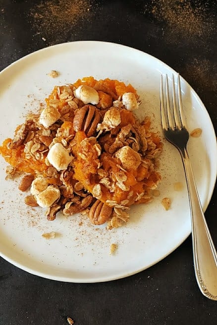 Sweet potato casserole with marshmallows and pecan streusel served on a white dessert plate.