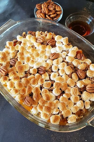 A baking dish full of toasted marshmallows and pecans served over casserole.