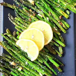 Stalks of tender green roasted asparagus served with lemon wedges ad seasoning.