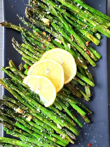 Stalks of tender green roasted asparagus served with lemon wedges ad seasoning.