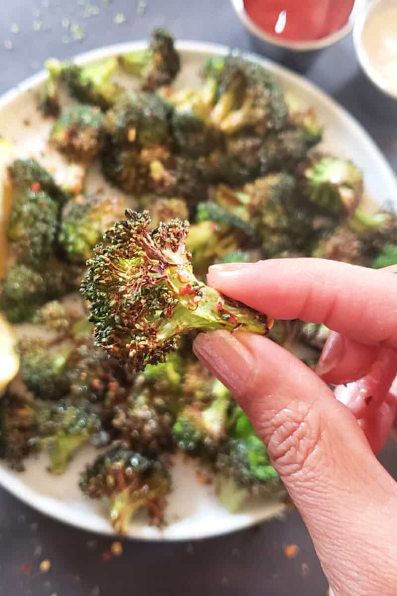 A hand holding a crispy broccoli floret made in the air fryer.