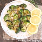 Crispy air fryer broccoli florets garnishes with lemon wedges and rosemary served on a white dinner plate.