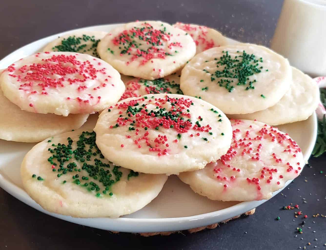 Soft and buttery cookies garnished with red and green sprinkles are stacked on white dessert plate.