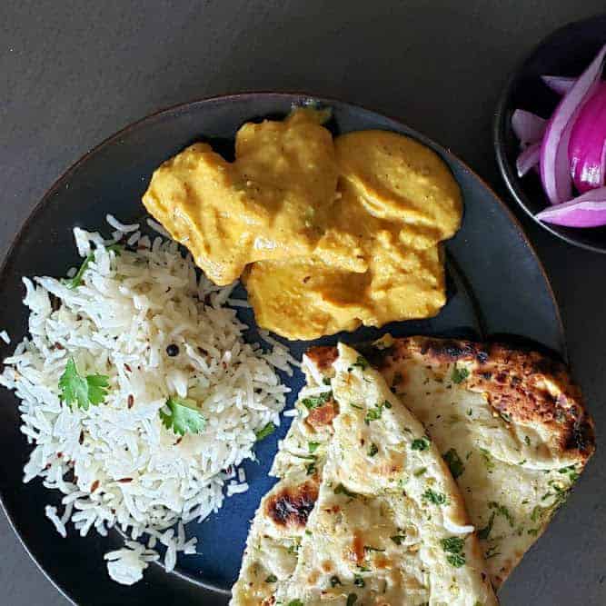 An overhead image of a dinner plate filled with paneer curry, seasoned rice and garlic naan.