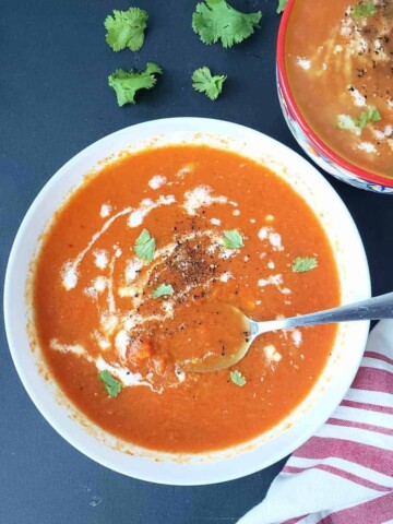 Two soup bowls filled with healthy carrot ginger soup. This vegan soup is served for dinner with optional garnishes