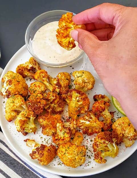 A hand holding a curry flavored cauliflower nugget dipping in the sauce.