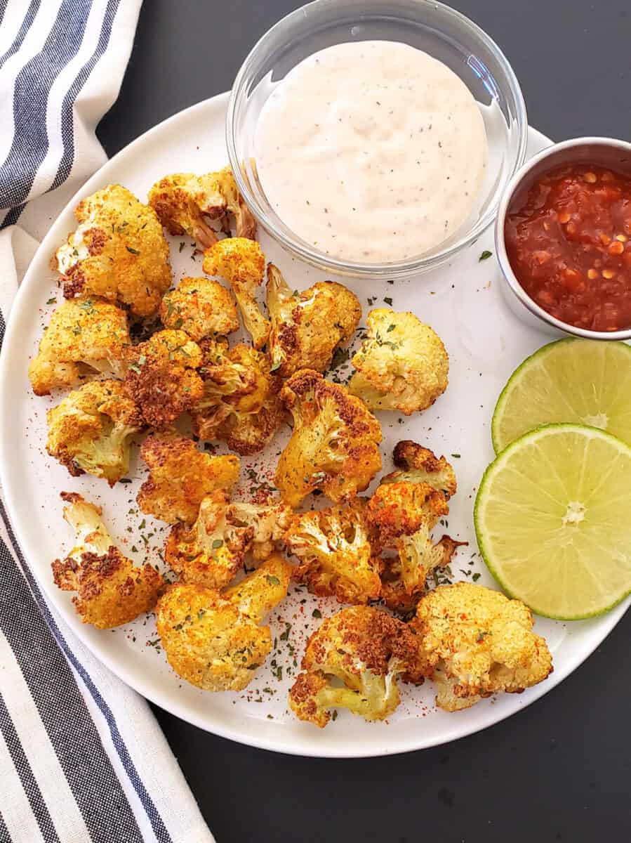 A white serving plate full f crispy cauliflower pieces and curry seasoning garnishes served for side dish or appetizer. 