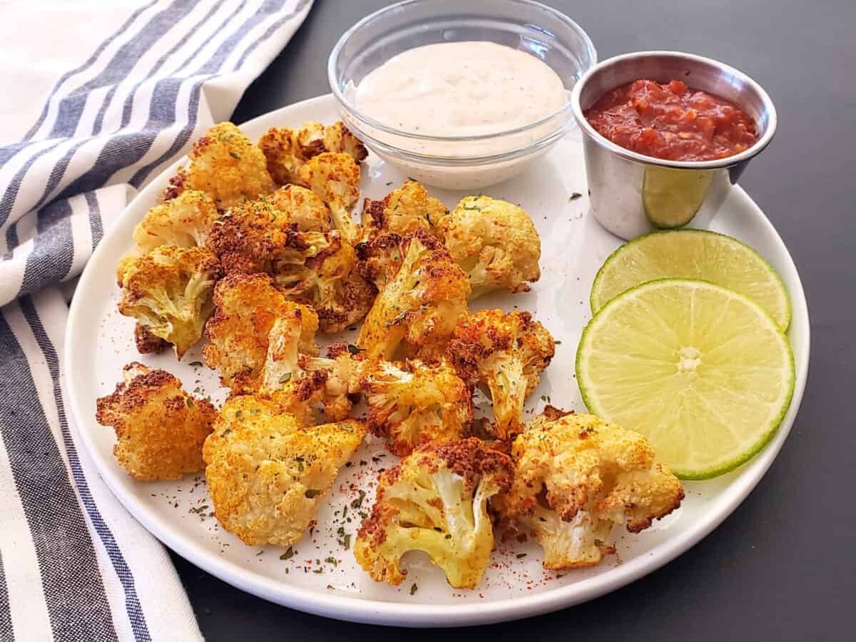 Crispy cauliflower florets with curry seasoning served with dipping sauces and lemon wedges as garnishes. 