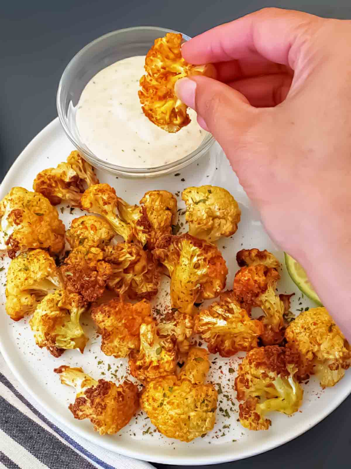 A hand holding a curry cauliflower nuggets dipping in the sauce.