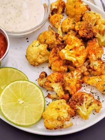A white serving plate full of crispy air fryer curry cauliflower served as a side dish or appetizer.
