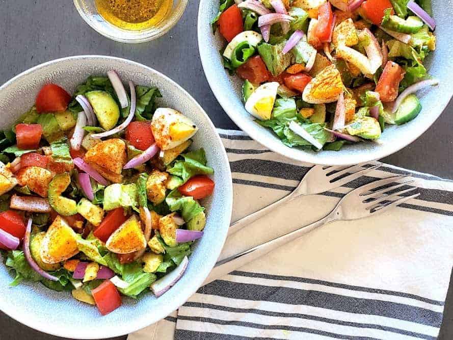 An overhead image of two salad bowls filled with colorful salad and a bow of dressing on the side.