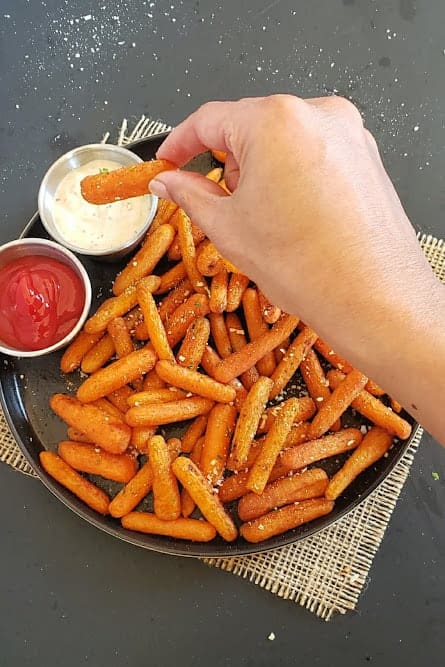 A hand dipping oven roasted carrot stick in the creamy sauce.