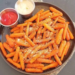 A serving platter full of roasted arrot sticks along with creamy dips.