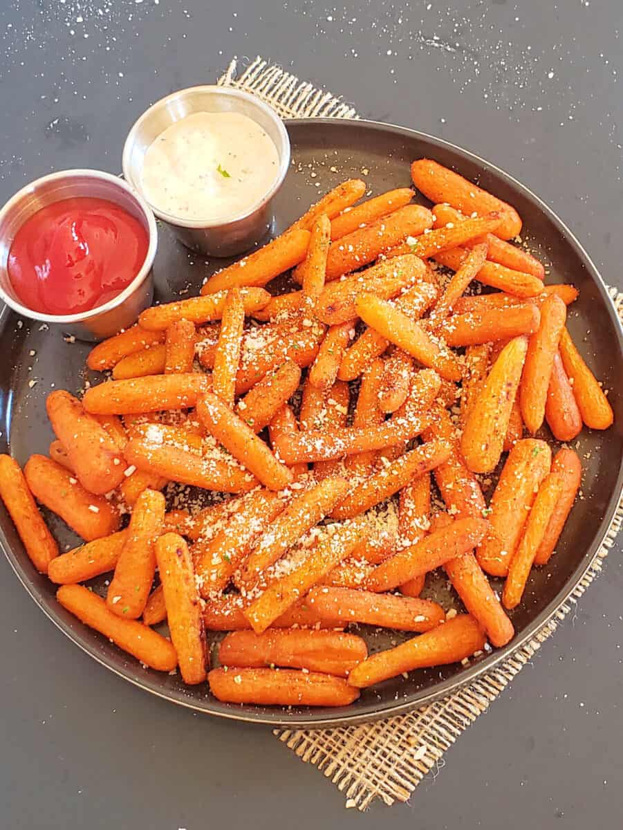 A serving platter full of roasted arrot sticks along with creamy dips.