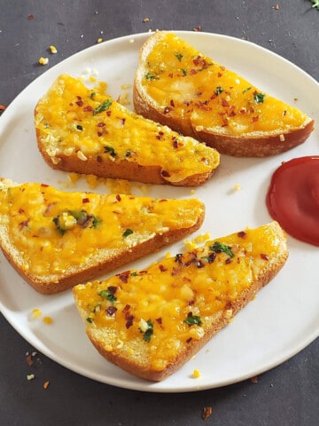 Garlic Toast made in air fryer cut into triangle and served with a dip on the round platter.