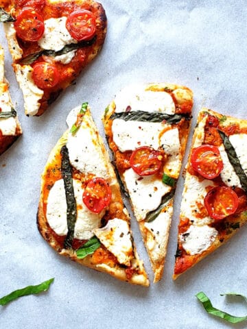 Air fryer naan bread pizza with tomatoes, cheese and basil cut into triangles on baking sheet.