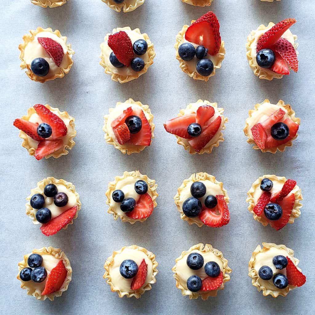 Phyllo Cups filled with cheesecake and topped with berries served on a tray. 