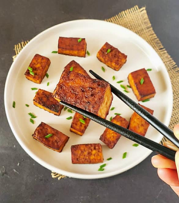 A chopstick holding piece of caramelized smoked tofu.