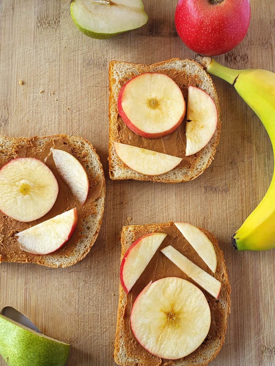 Banana, pear, and apples stacked on peanut butter sandwich.