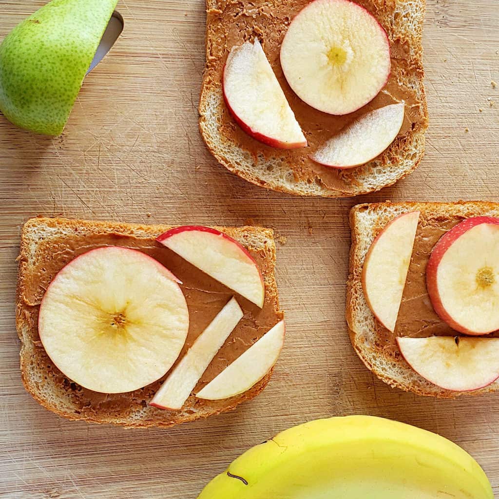 Three peanut butter sandwiches with different fruit toppings.