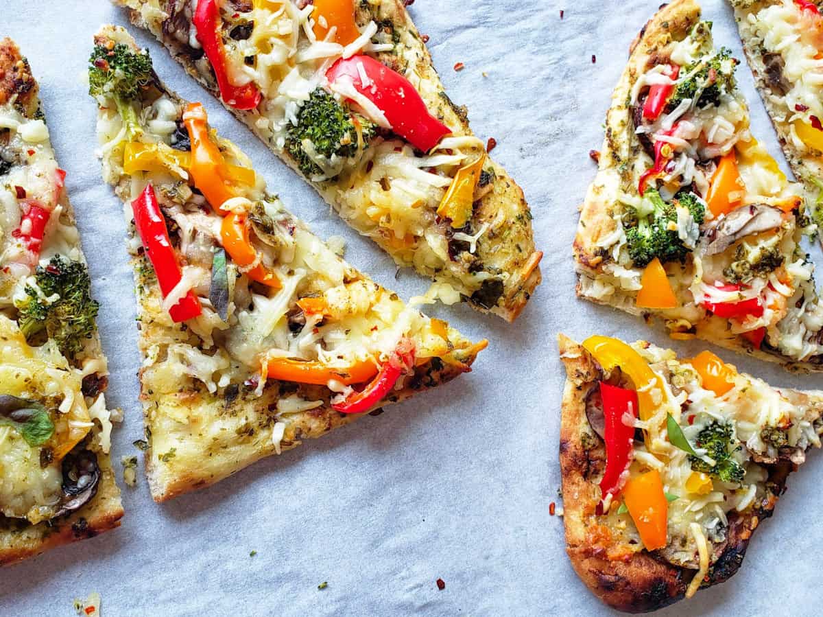 Pieces of naan pizza with pesto and colorful vegetables.