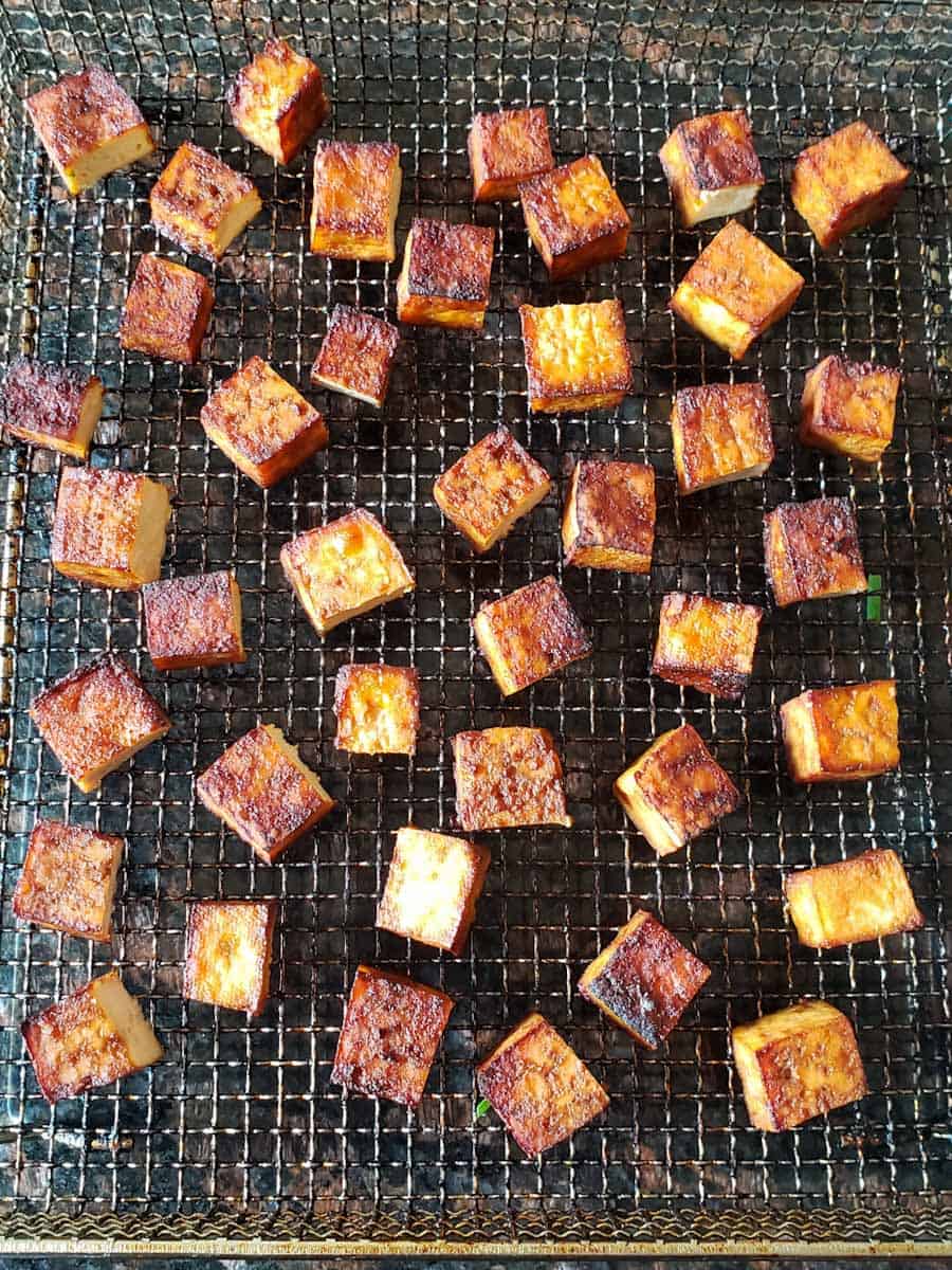 Golden brown tofu bites on air fryer basket. 