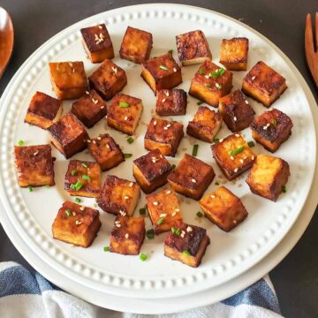 Crispy tofu cubes with garnishes served on dinner plate.