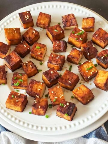 Crispy tofu cubes with garnishes served on dinner plate.