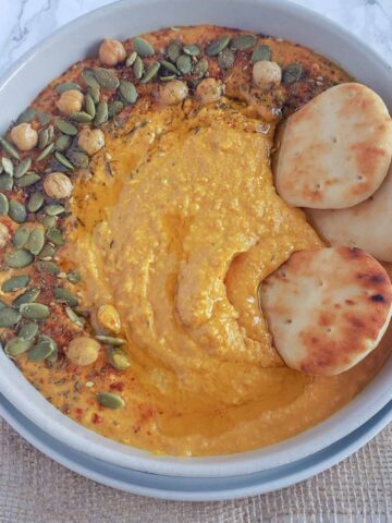 Creamy pumpkin hummus served with garnishes and dippers.