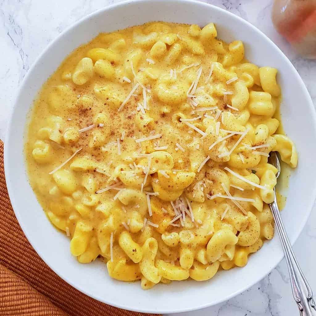 Delicious and healthy pumpkin mac and cheese served in a white bowl with fork.