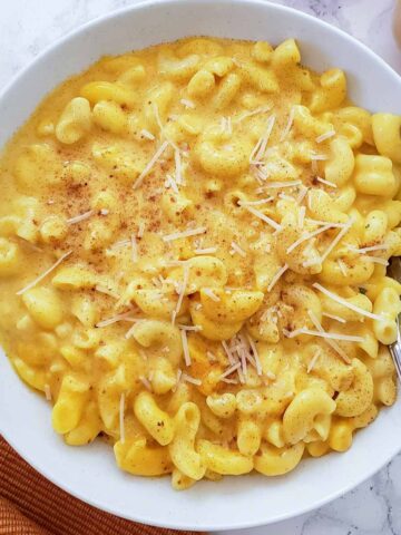Delicious and healthy pumpkin mac and cheese served in a white bowl with fork.