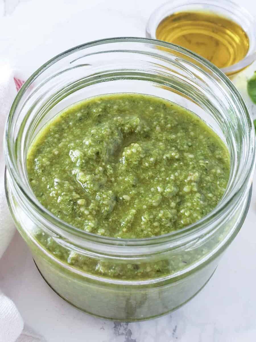 A glass jar full of creamy herby pesto sauce made with basil and walnuts.