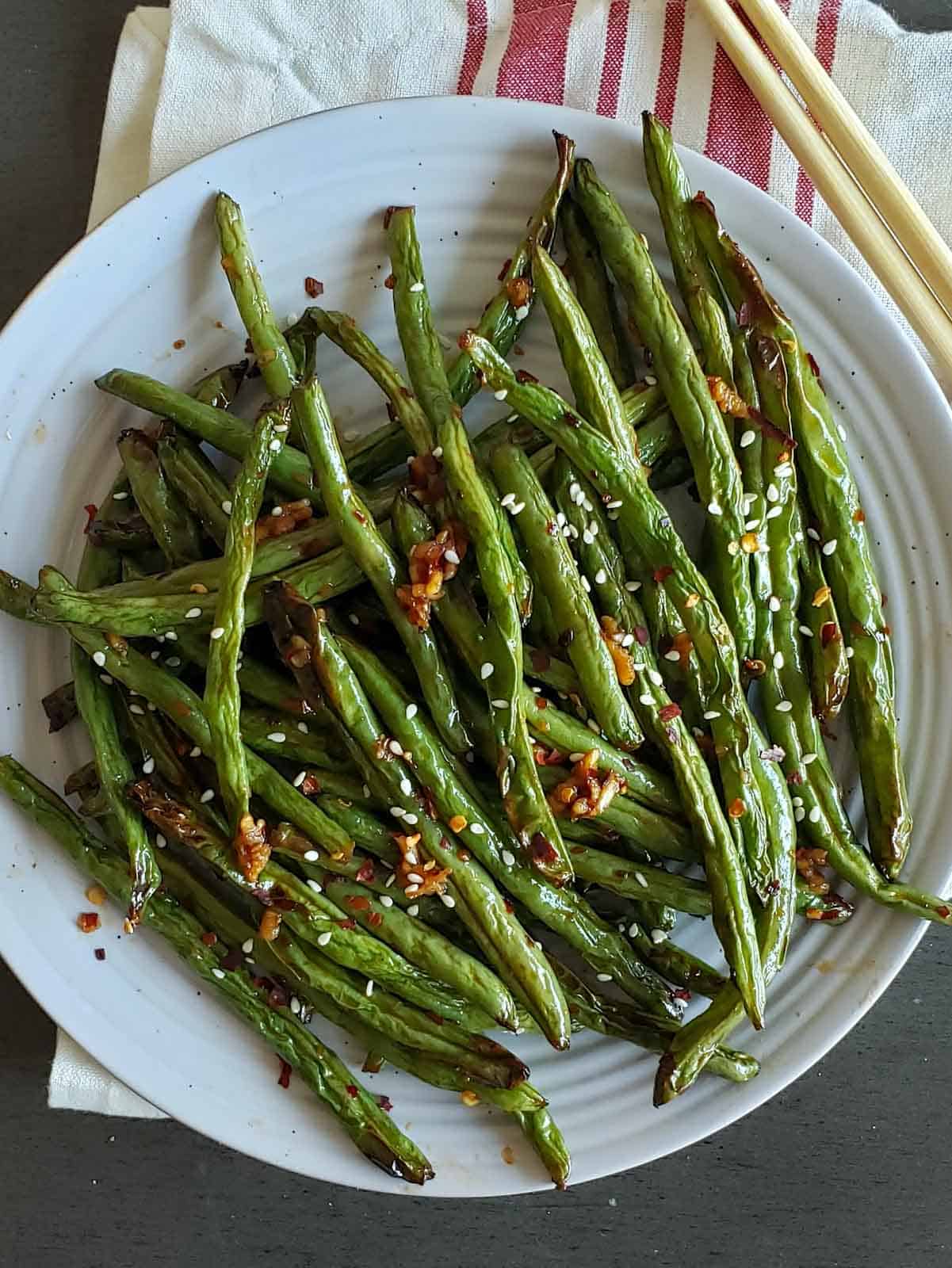 Spicy air fryer green beans served in a plate with garnishes.