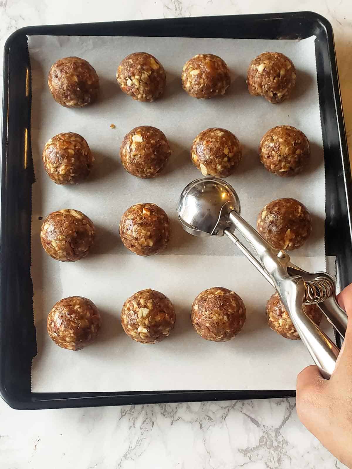 A cookie scoop dropping the energy ball dough on the baking sheet.