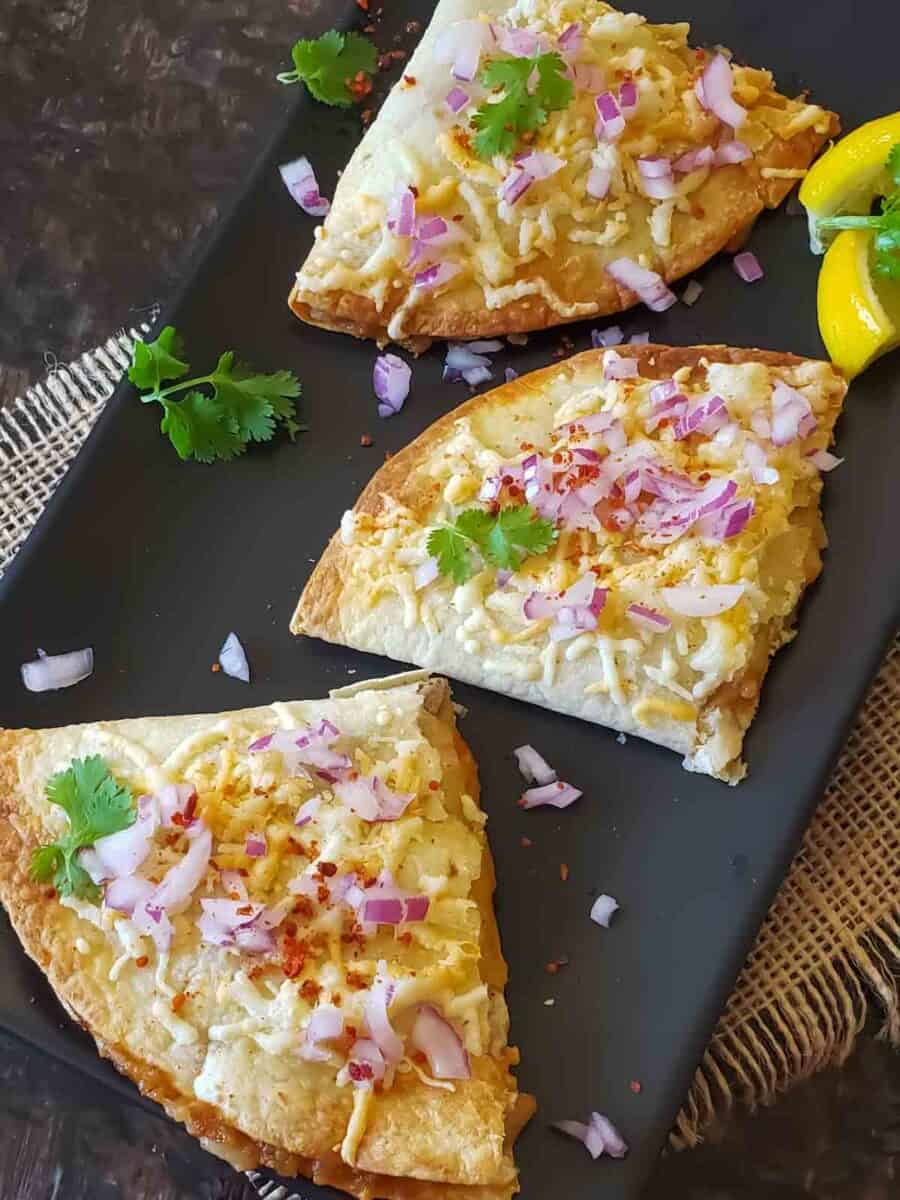Pav Bhaji Quesadillas, the fusion recipe,  made by combining Indian street food pav bhaji and Mexican cheese quesadillas, served with garnishes on the black serving platter. 