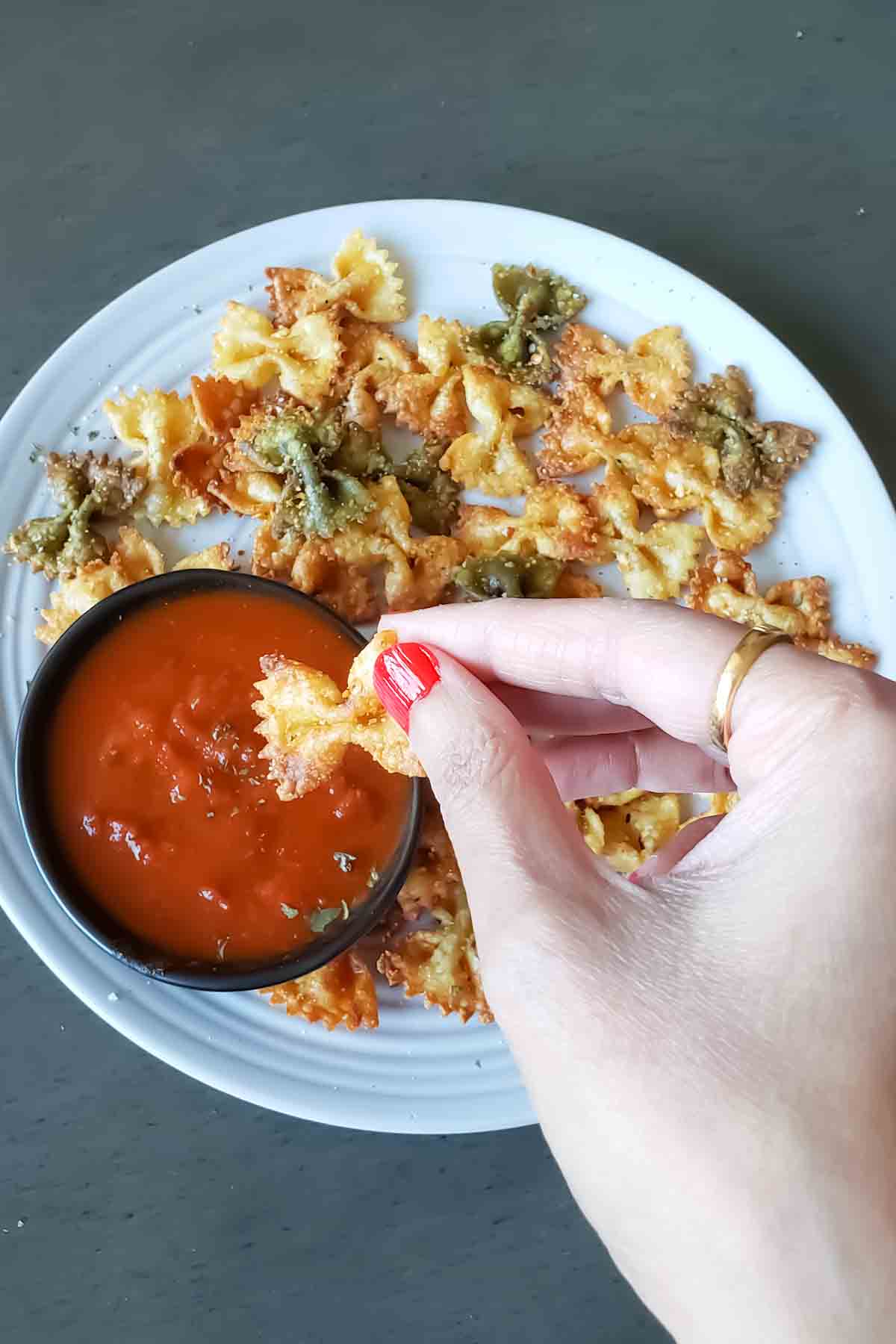 A hand holding a air fried pasta chip and dipping into sauce.
