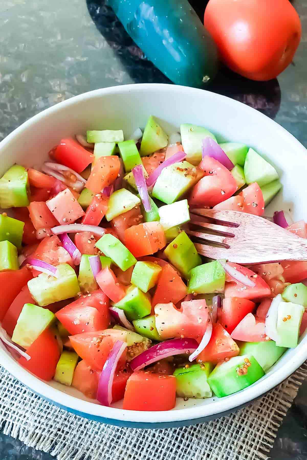 Balsamic cucumber and tomato salad served with wooden fork.